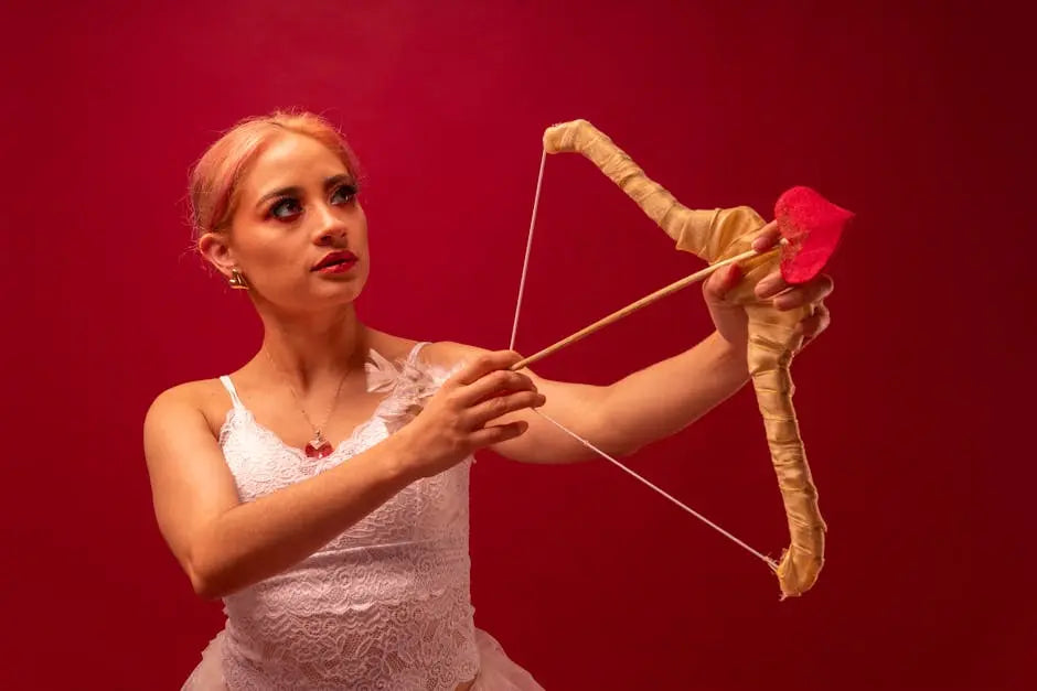 Young woman with pinkish hair holds a decorative bow and arrow. She wears a white lace bodice resembling ballet attire. The bow is gold, and the arrow has a heart-shaped tip.