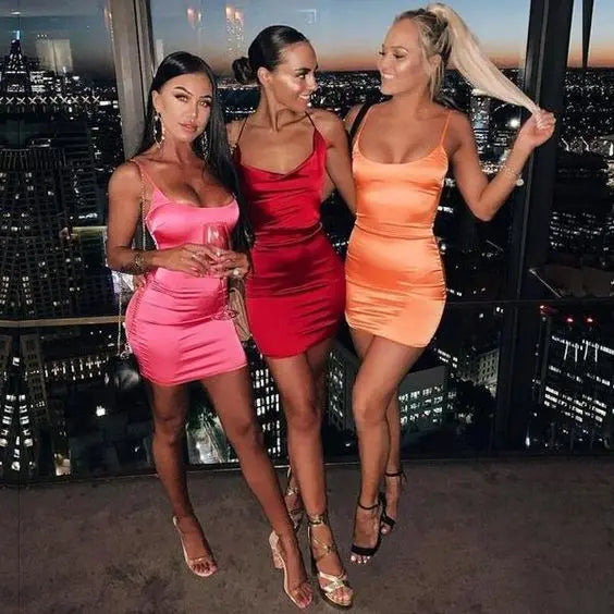 A group of women in dresses, smiling and posing for a picture; one woman in a pink dress holds a glass of wine.