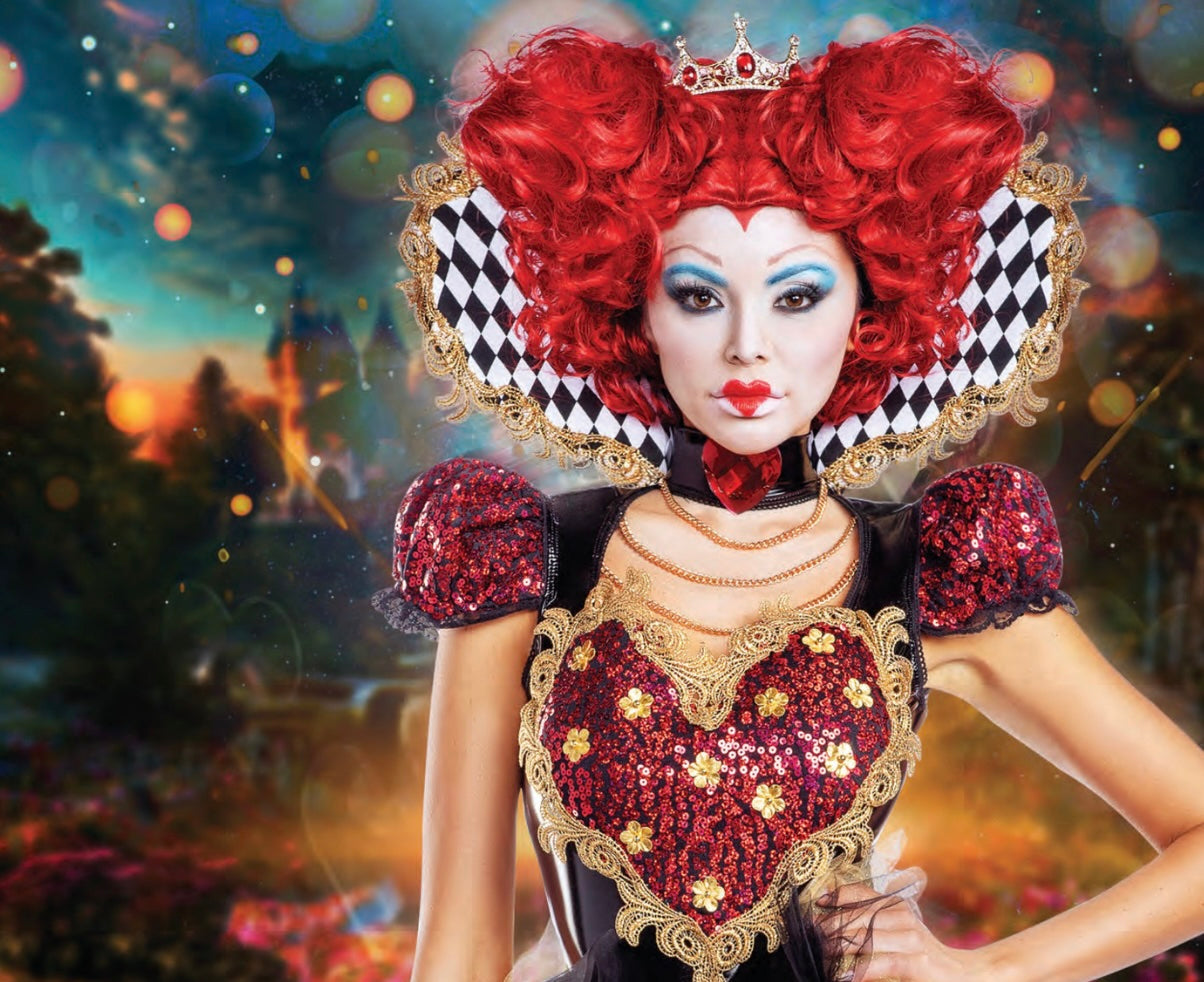 A model in a Queen of Hearts costume with a red curled wig, jeweled tiara, dramatic makeup, flared collar, sequined bodice, heart motif, and layered necklaces.