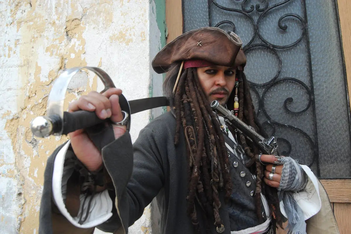 A man dressed as a pirate, wearing a hat and holding both a sword and a gun, standing outdoors.
