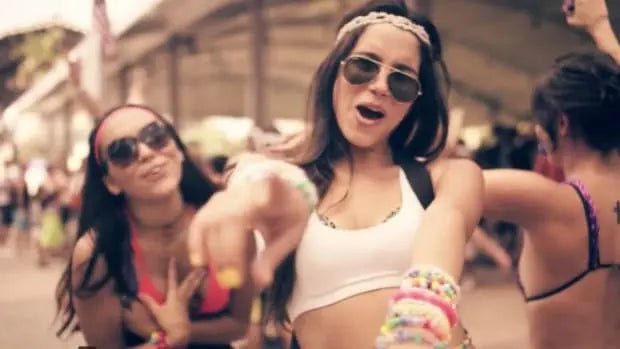 A woman wearing sunglasses and a pink headband, smiling and pointing, with a close-up view of her face visible.